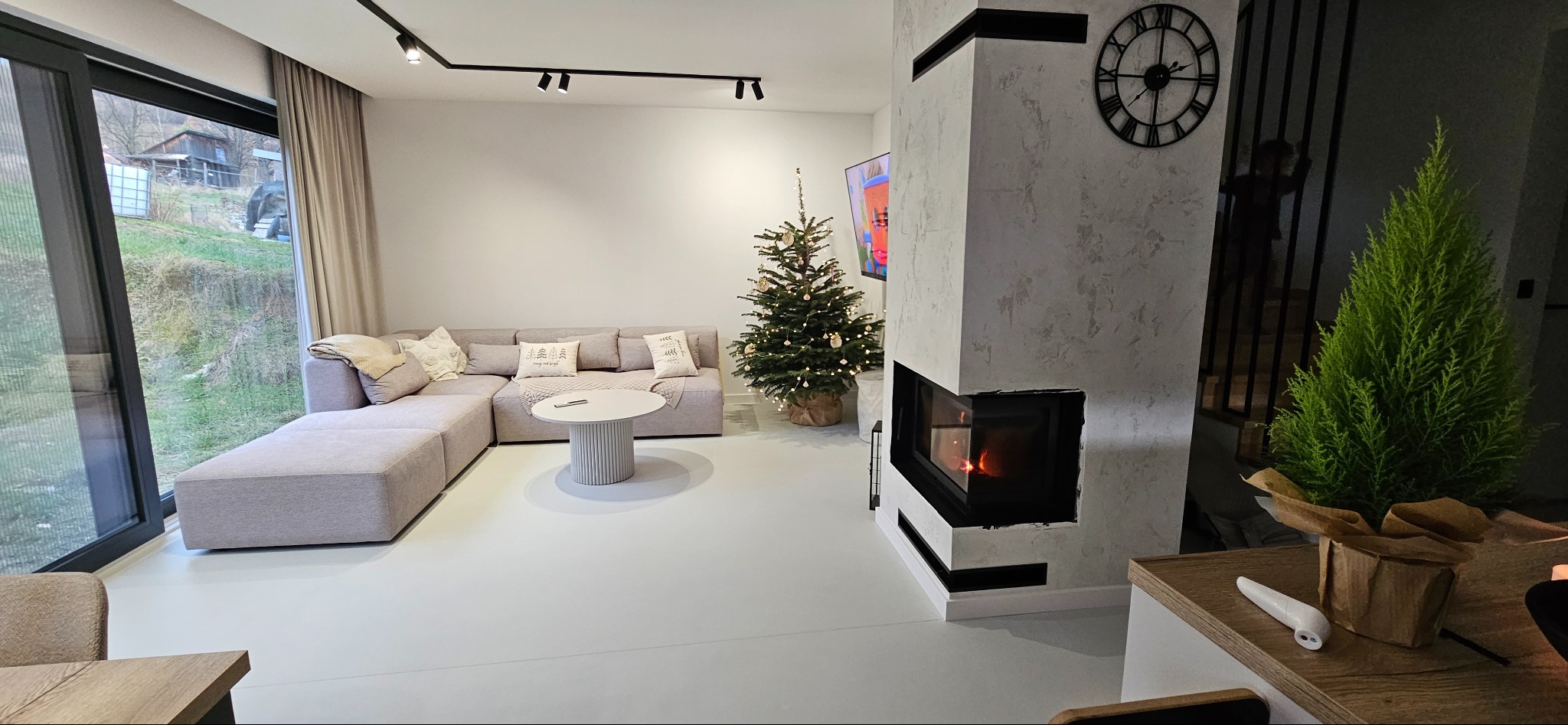 Jasnoszara posadzka żywiczna w nowoczesnym salonie z kominkiem, szarą sofą narożną i dekoracjami świątecznymi.