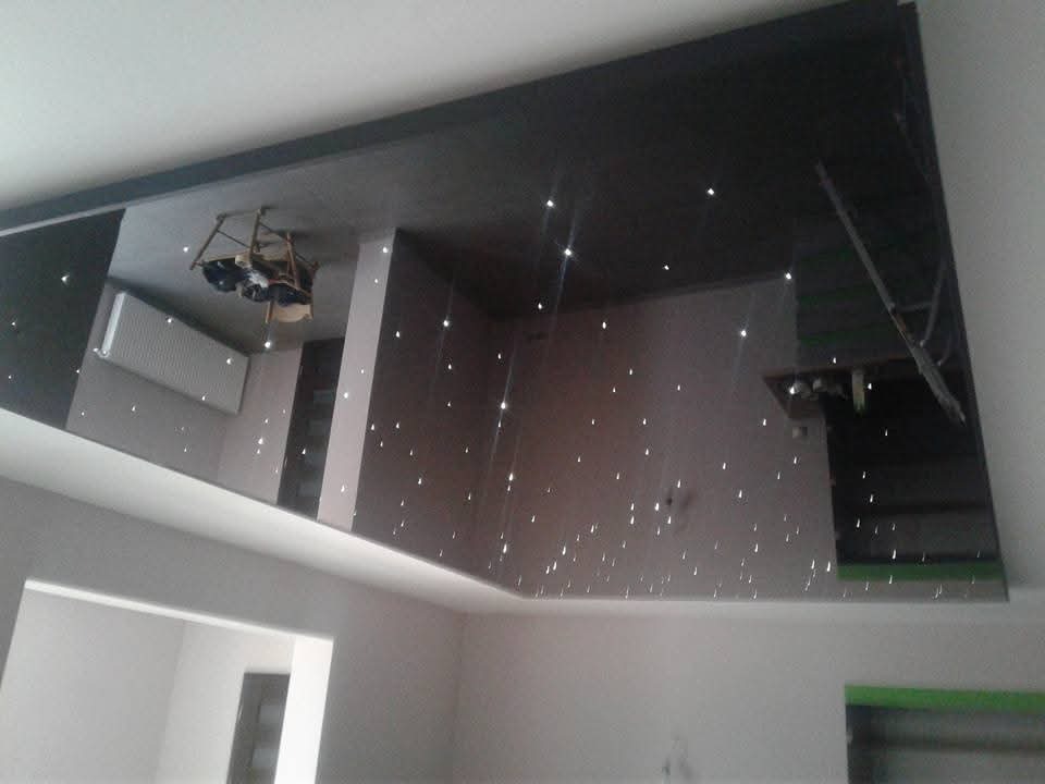 Błyszczący, czarny sufit z efektem gwiazd, odbijający wnętrze pokoju, w tym grzejnik i sprzęt oświetleniowy.