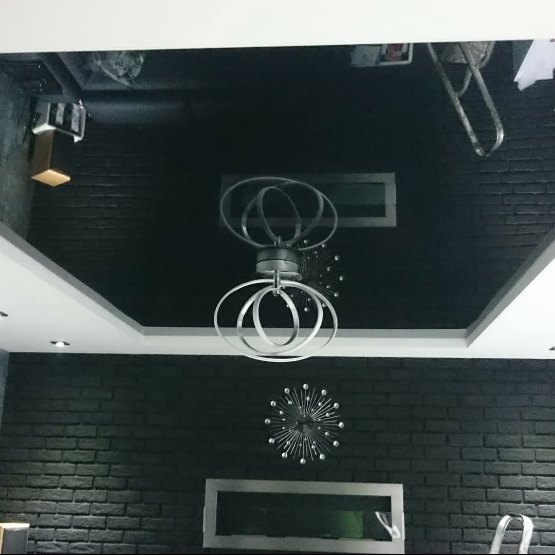 Czarne ściany z cegły i czarny błyszczący sufit podwieszany z nowoczesnym oświetleniem w kształcie pierścieni i dekoracyjnymi elementami.