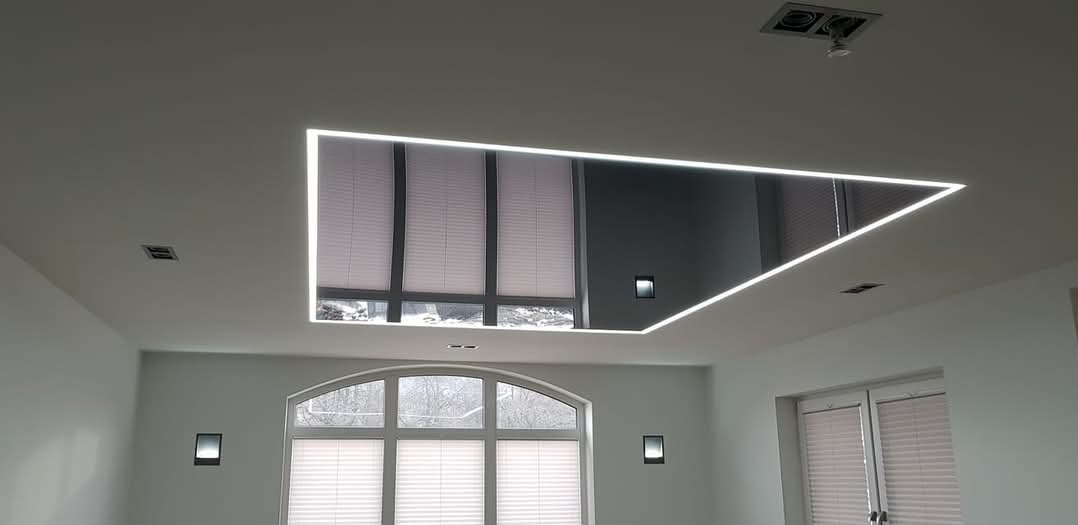 Nowoczesny salon z podwieszanym sufitem z lustrzanym panelem i oświetleniem LED, widok na okna z żaluzjami.