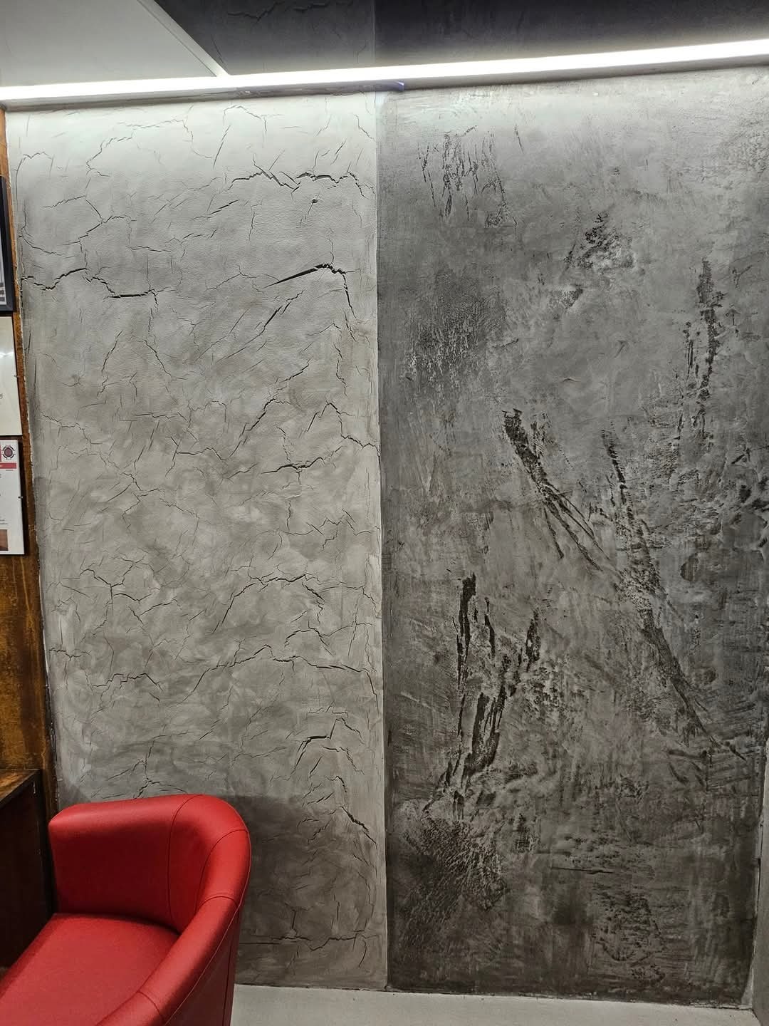 Dwa panele ścienne z dekoracyjnym tynkiem: po lewej jaśniejszy z efektem spękań, po prawej ciemniejszy z nieregularnymi wzorami, oświetlone listwą LED u góry, obok czerwone krzesło.