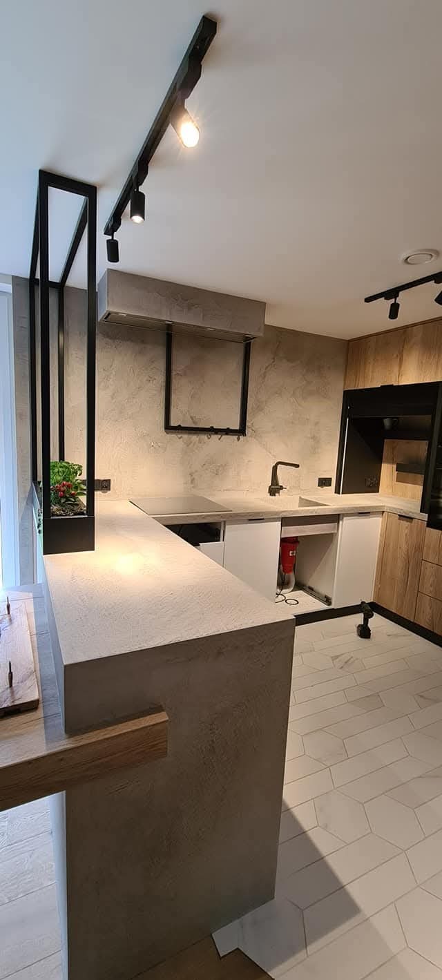 Nowoczesna kuchnia z betonowym blatem, oświetleniem szynowym i podłogą z płytek w kształcie rombów.