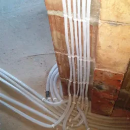 Rzut z góry na wiązkę białych rurek instalacyjnych, przymocowanych do surowej, ceglanej ściany w trakcie montażu.