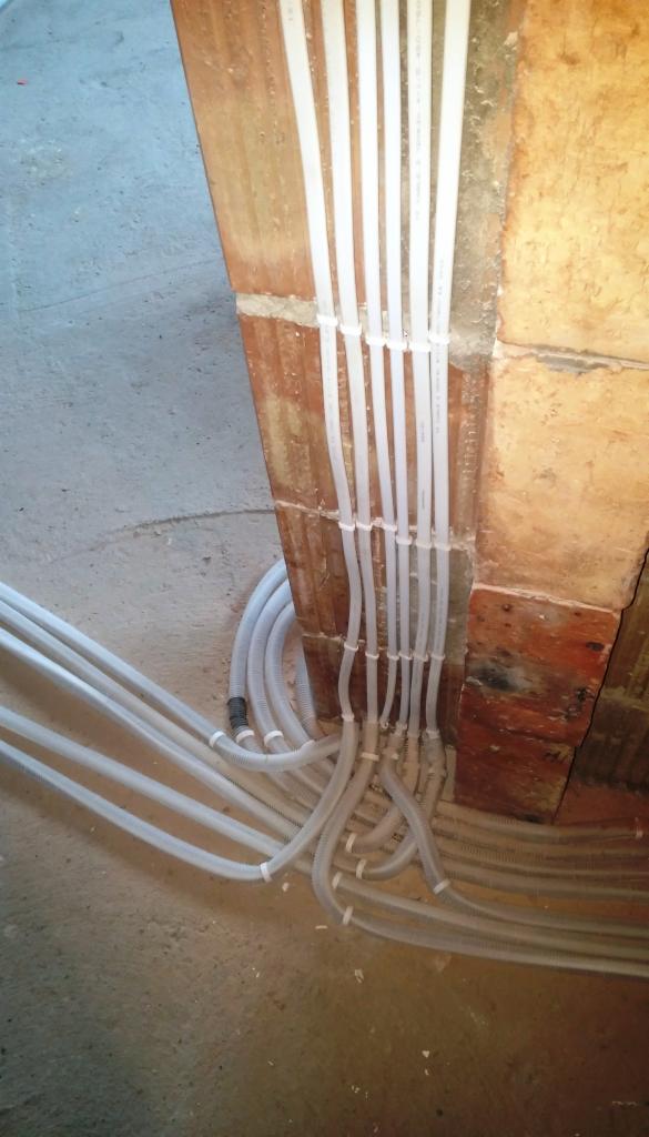 Rzut z góry na wiązkę białych rurek instalacyjnych, przymocowanych do surowej, ceglanej ściany w trakcie montażu.