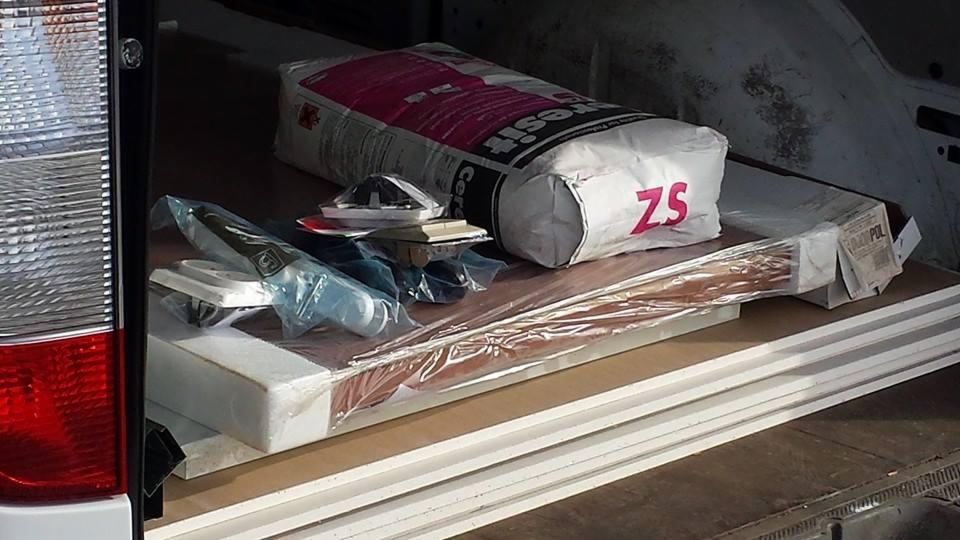 Wnętrze busa załadowane materiałami budowlanymi: worek cementu Cersit, płyty styropianowe, listwy przypodłogowe i akcesoria, gotowe do transportu.