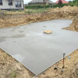 Wylana płyta fundamentowa na budowie domu jednorodzinnego, widok z góry. Widoczne szalunki, wykop i narzędzia.