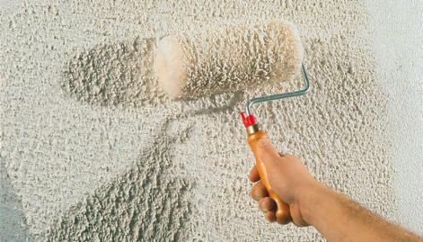 Nakładanie tynku strukturalnego na ścianę za pomocą wałka z długim włosiem, widoczna struktura nałożonej warstwy.