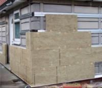 Fragment ściany budynku w trakcie ocieplania wełną mineralną, widoczne płyty wełny przymocowane do elewacji, elementy konstrukcji nośnej pod przyszłe wykończenie tynkiem.