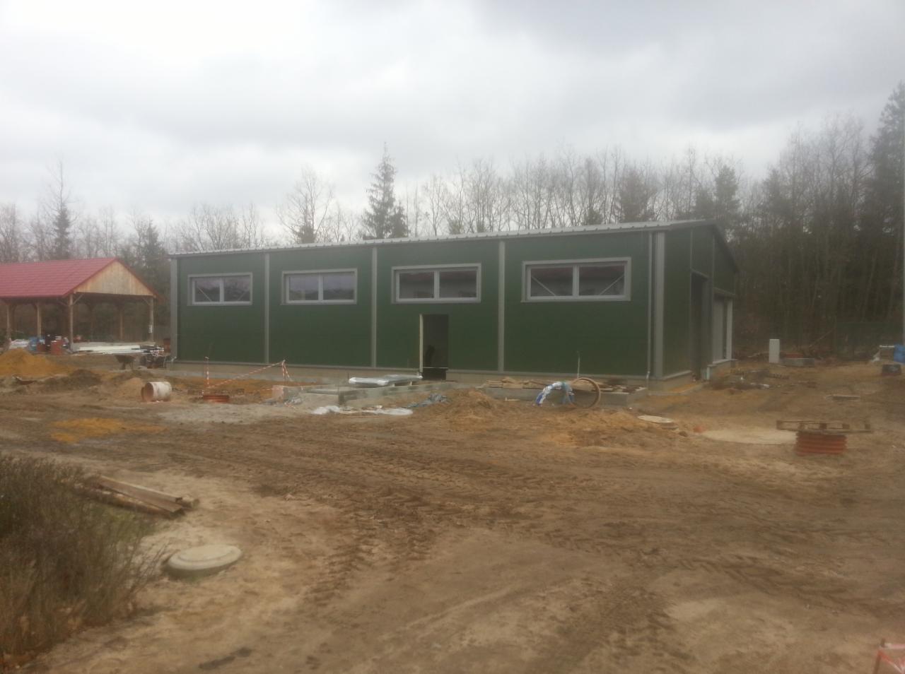 Budowa chłodni w Tarchalicach: zielony budynek z oknami na etapie fundamentów, widoczne materiały budowlane i teren przygotowany pod inwestycję.