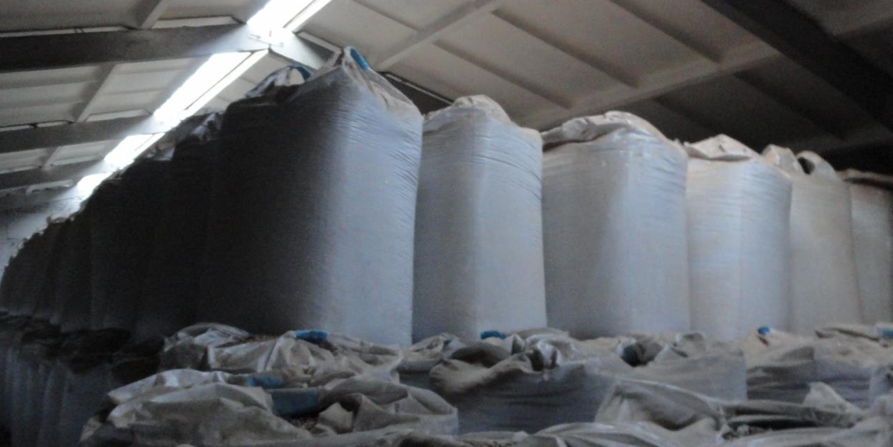 Magazyn pełen dużych, białych worków z pelletem drzewnym, ułożonych w rzędach pod sufitem hali.