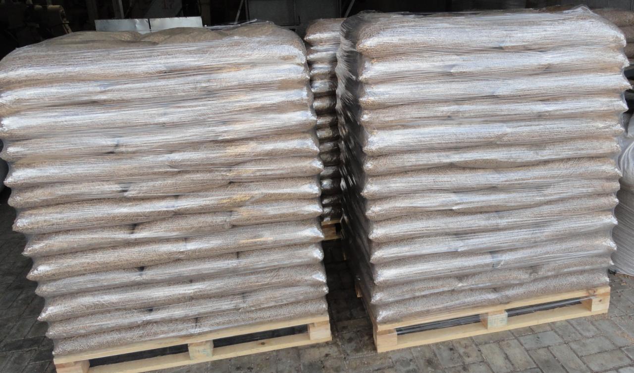 Dwa stosy worków z pelletem drzewnym 6mm, ułożone na drewnianych paletach i owinięte folią stretch.