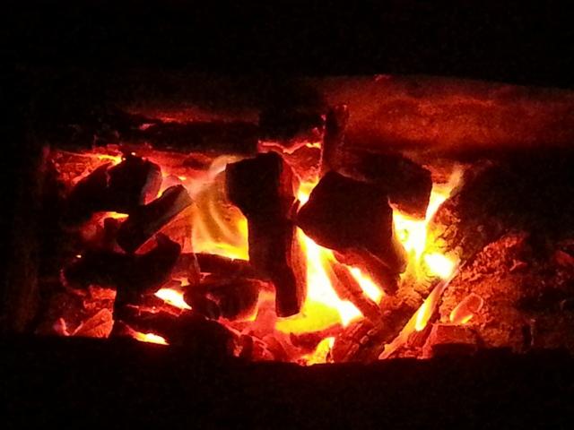 Żarzące się bryłki węgla drzewnego z widocznym płomieniem w ciemnym otoczeniu.