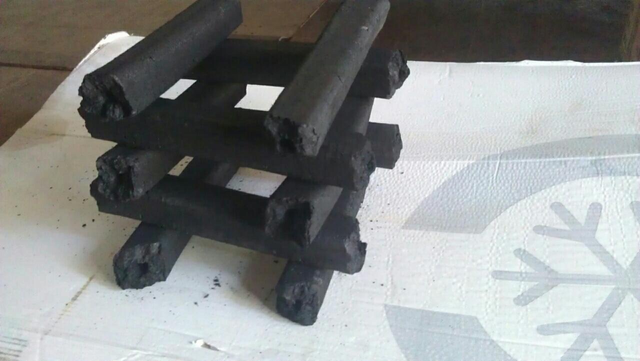 Ułożone w stos brykiety węglowe o cylindrycznym kształcie, widoczne pęknięcia i nierówności na powierzchni, tło stanowi białe podłoże z delikatnym wzorem.