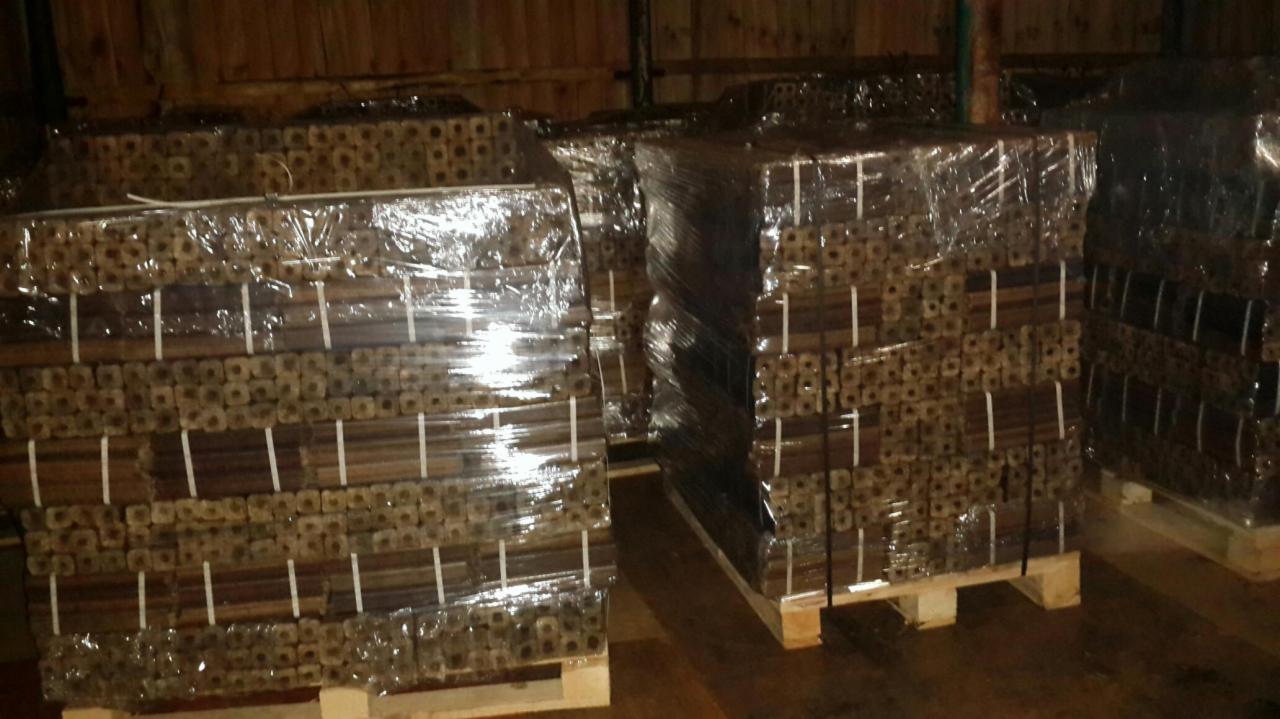 Pakiety brykietu drzewnego PINI & KAY, owinięte folią i ułożone na paletach, składowane w magazynie w Bestwinie. Widoczne charakterystyczne otwory w brykiecie.