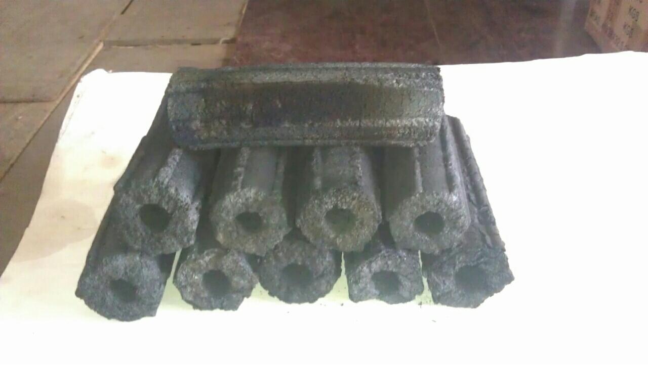 Stos brykietów węglowych o cylindrycznym kształcie z otworem w środku, ułożonych na białym podłożu, widoczne tekstury i nierówności powierzchni w słabym oświetleniu.