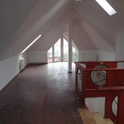 Przestronne poddasze z oknami dachowymi i drewnianą podłogą, wykończone w bieli i błękicie, z elementami dekoracyjnymi z drewna i szkła. Widok na zewnątrz.