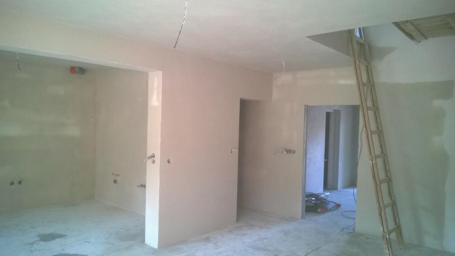 Wnętrze po tynkowaniu: gładkie, jasne ściany, widoczne instalacje elektryczne, drabina oparta o ścianę, przygotowane do dalszych prac wykończeniowych.