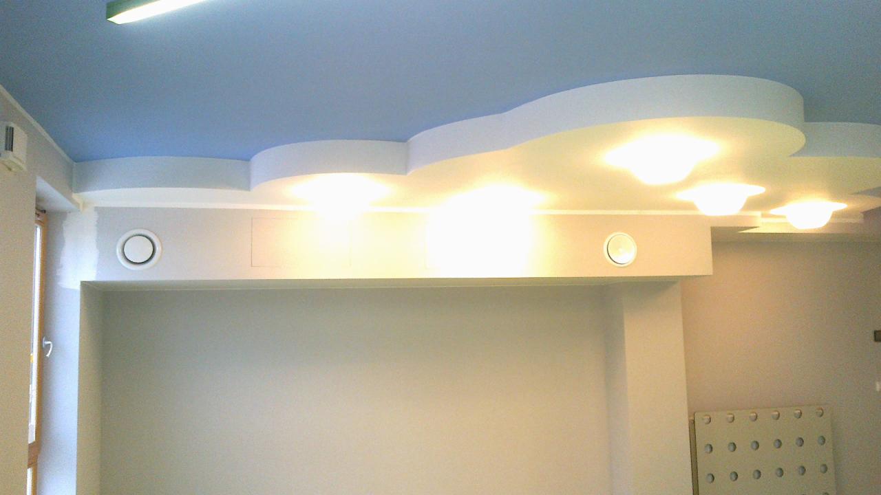 Dekoracyjny sufit podwieszany z płyt karton-gips, oświetlenie punktowe. Błękitne tło sufitu, białe elementy dekoracyjne. Widoczny fragment ściany z kratką wentylacyjną.