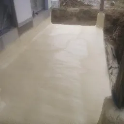 Świeżo nałożona, gładka warstwa izolacji piankowej na fundamentach budynku w trakcie budowy, widoczne zabezpieczenia folią i ziemia w wykopie.