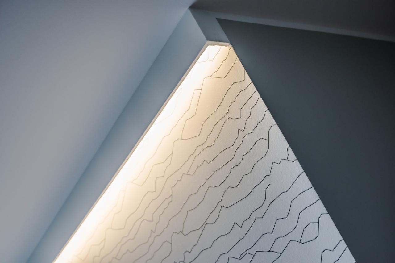 Narożnik sufitu z oświetleniem LED i tapetą z abstrakcyjnym wzorem linii, pomalowany na szaro.