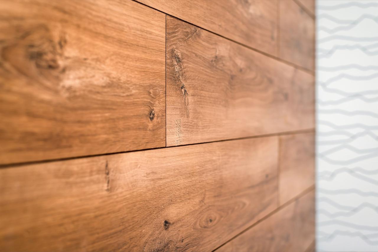 Drewniana okładzina ścienna z widocznymi detalami słojów i sęków, sąsiadująca z białą ścianą z delikatnym, szarym wzorem falistym.