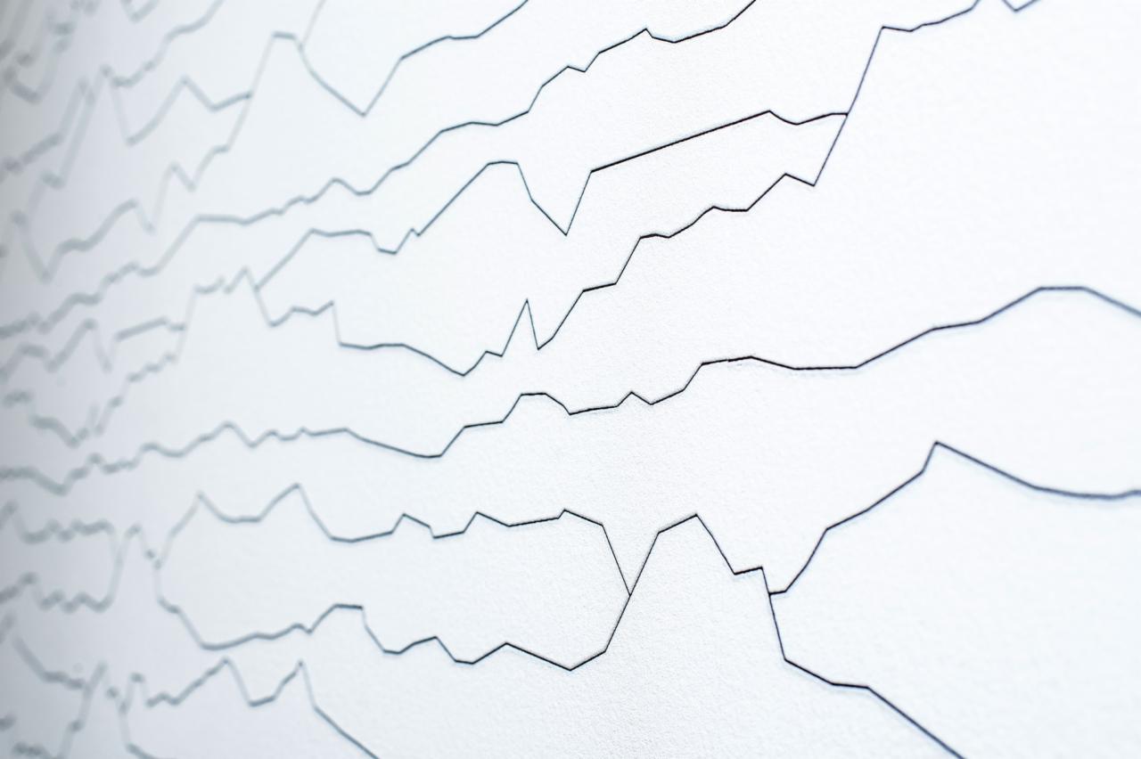 Abstrakcyjne malowanie na ścianie w postaci poziomych linii z ostrymi załamaniami, przypominające wykres, wykonane cienką czarną farbą na białym tle.