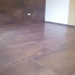 Brązowe, prostokątne płytki podłogowe ułożone w regularny wzór, z widocznymi fugami, na tle ściany w kolorze ciemnego brązu oraz białej ściany z zabudowaną szafką.