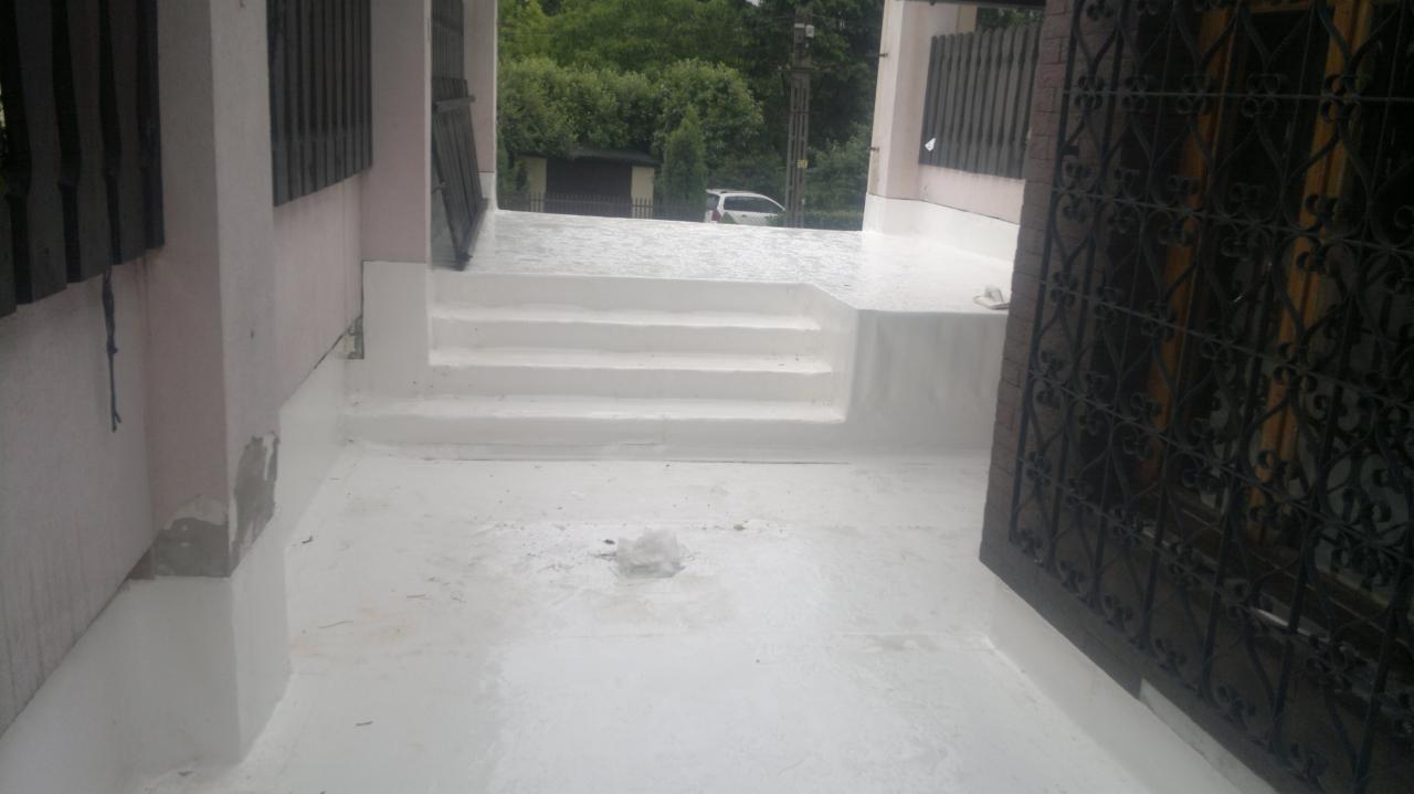 Biała hydroizolacja balkonu z trzema schodami, widok z góry. Świeżo pomalowana powierzchnia, czyste linie, barierka z metaloplastyki po prawej.