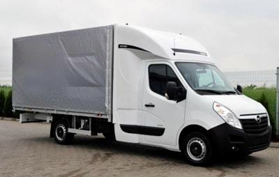 Biały samochód dostawczy z szarą plandeką na parkingu, widok z boku, czyste tło, lekko pochmurne niebo.