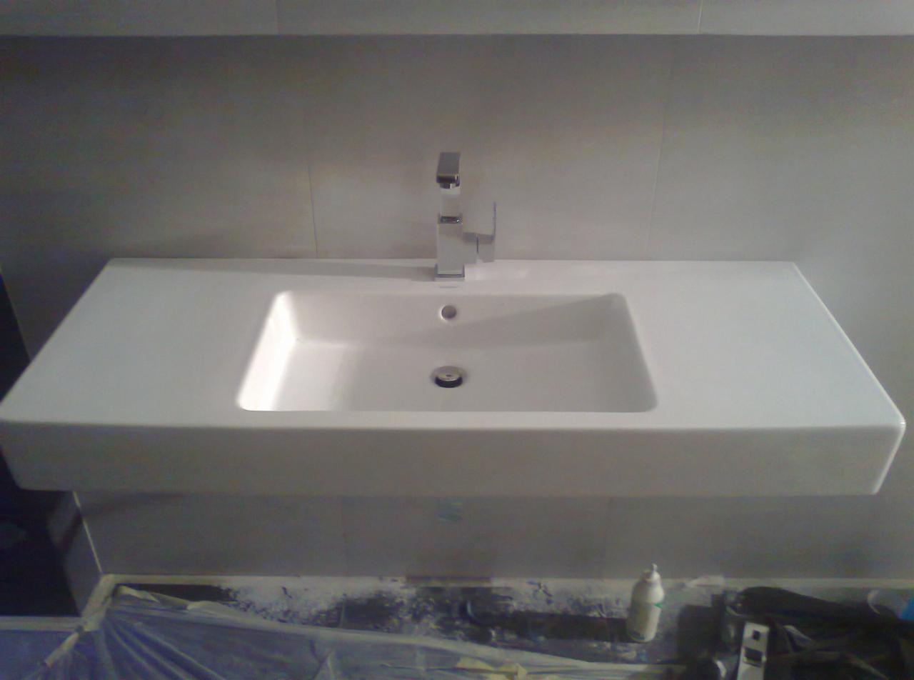 Nowoczesna, biała umywalka z chromowaną baterią, zamontowana na płytkach. Widoczne narzędzia i zabezpieczenia pod umywalką, sugerujące świeży montaż.