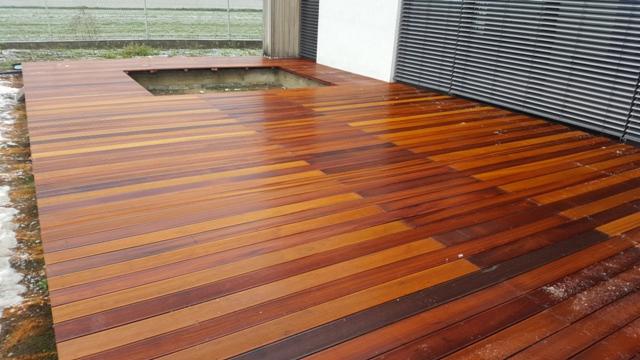 Świeżo położony taras z egzotycznego drewna z wycięciem na oczko wodne, widoczny fragment ogrodu z resztkami śniegu.