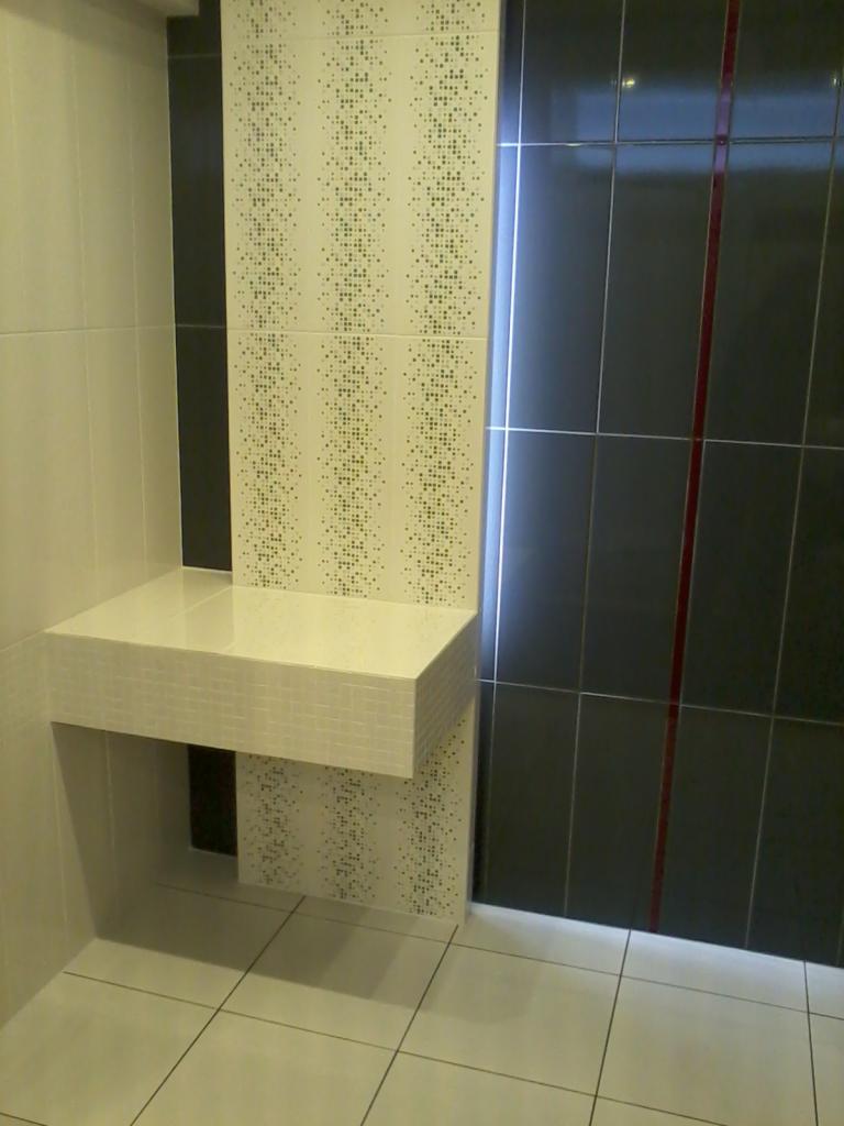 Nowoczesna łazienka z minimalistyczną umywalką obłożoną mozaiką, kontrastujące płytki w odcieniach bieli, szarości i czerni, pionowe pasy dekoracyjne z drobnym wzorem.