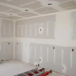 Wnętrze pokoju w trakcie prac wykończeniowych: ściany i sufit pokryte płytami kartonowo-gipsowymi, widoczne łączenia wymagające szpachlowania, drabina w pomieszczeniu.