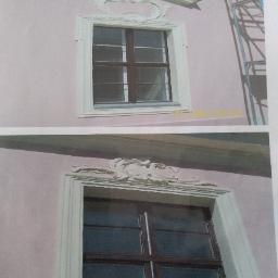 jorbud jerzy pielak - Dwa okna z ozdobnymi, jasnymi obramieniami i dekoracyjnymi elementami nad oknami na różowej elewacji budynku, widoczne rusztowanie z prawej strony.