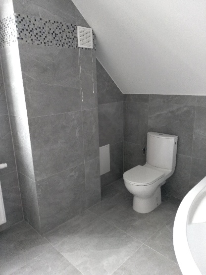 Szara łazienka na poddaszu z toaletą, wentylatorem i mozaiką nad płytkami, wykończona w nowoczesnym stylu.