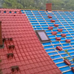 Częściowo pokryty dach z dachówką w Czernichowie. Widoczna membrana, łaty i ułożone dachówki. Fragment komina z cegły.