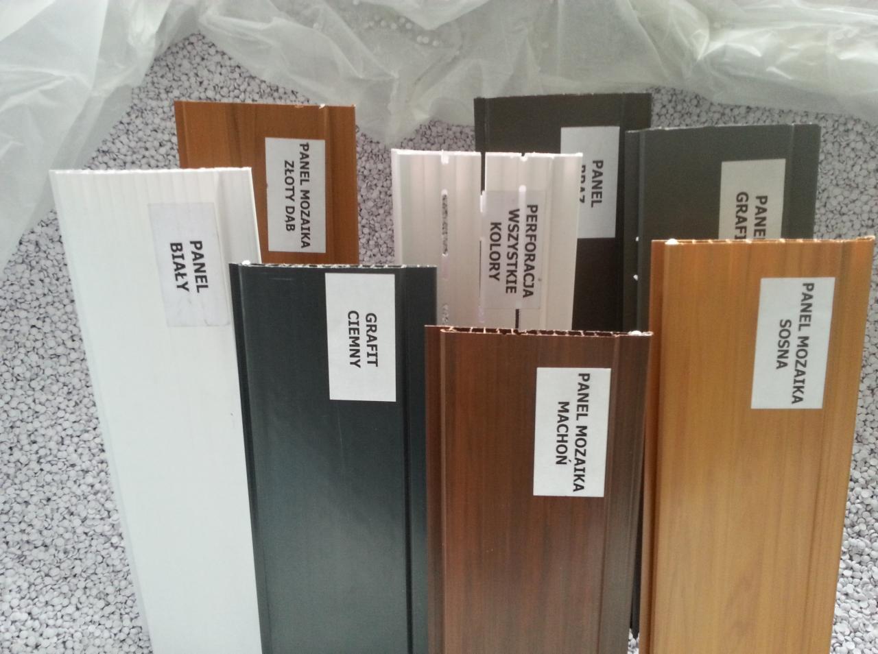 Próbki paneli mozaikowych w różnych kolorach i wzorach, w tym złoty dąb, sosna, grafit, machoń, biały, ciemny grafit, prezentowane na tle białych granulek.