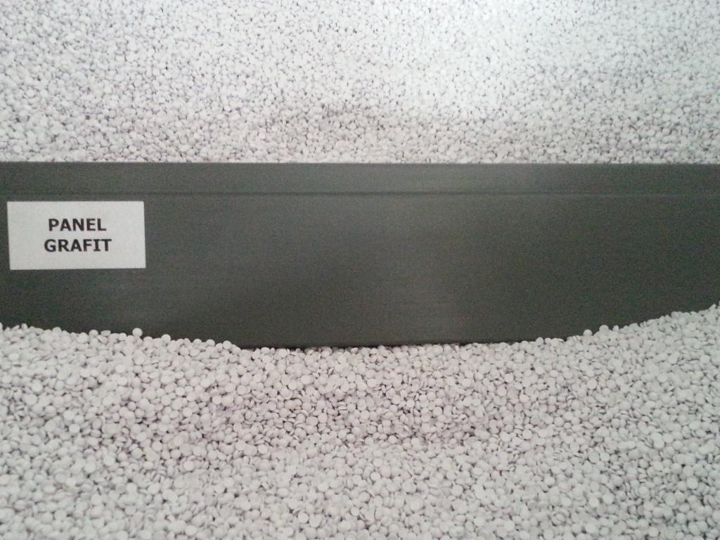 Grafitowy panel z etykietą 'Panel Grafit' otoczony białym granulatem. Materiał budowlany prezentowany na tle drobnych kulek.