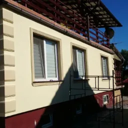 Wykończona elewacja domu z dekoracyjnymi elementami narożnymi i wokół okien, widoczne rusztowania.