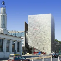 Nowoczesny budynek biurowy z perforowaną elewacją w Poznaniu, widoczny z perspektywy ulicy, z charakterystyczną wieżą w tle.