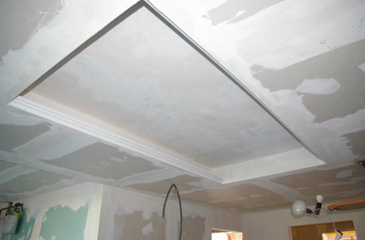 Sufit z płyt gipsowo-kartonowych w trakcie szpachlowania, widoczne łączenia i listwy dekoracyjne. Etap prac wykończeniowych w pomieszczeniu.