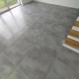 Szare, matowe płytki podłogowe ułożone w nowym domu w Tarnowskich Górach, widoczne fragmenty schodów z drewnianymi stopniami.