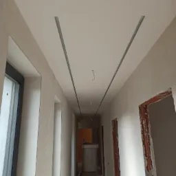 Korytarz w trakcie remontu z widocznymi profilami sufitowymi i świeżo nałożoną gładzią, przygotowany do dalszych prac wykończeniowych.