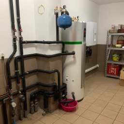 ATOM SYSTEM Tomasz Chrzanowski - Instalacja rekuperacji z zbiornikiem akumulacyjnym, widoczne rury w izolacji, manometry, zawory oraz półka z zapasami w tle.