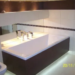 Wykończona łazienka z beżowo-brązowymi płytkami, podświetlaną wanną i toaletą. Widoczne lustro i armatura. Data w rogu zdjęcia.