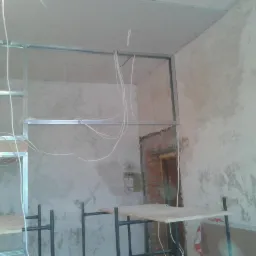 Konstrukcja z profili stalowych pod płytę gipsową na suficie i ścianie, widoczne przewody elektryczne. Fragment muru z cegły. Prace remontowe w trakcie.