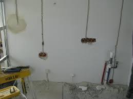 Biała ściana z wystającymi przewodami elektrycznymi i puszkami instalacyjnymi, przygotowana do dalszych prac wykończeniowych w remontowanym pomieszczeniu.