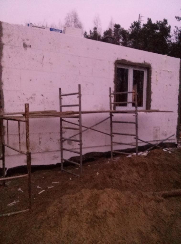 Budowa domu w Węgrowie. Ściany z białego materiału izolacyjnego, okno i rusztowanie. Widok na budynek w trakcie wznoszenia.