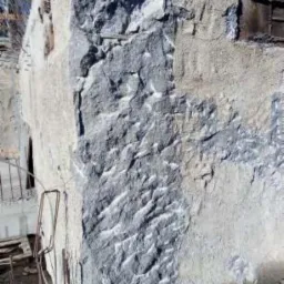 Fragment ściany z widocznymi śladami po wyburzeniu, odsłaniający surową strukturę materiału i resztki starego tynku.