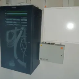 Szafa telekomunikacyjna z widocznymi kablami światłowodowymi, obok skrzynka rozdzielcza OPP 703 i biały panel, zamontowane na ścianie w surowym wnętrzu.